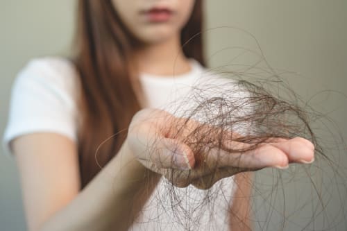 A young woman holds a clump of hair in her outstretched hand. Short depth of field, with focus on the clump of hair.