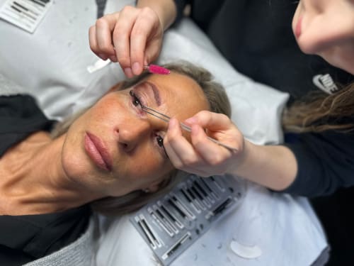 Grace Bayliss applying volume lashes, cat eye effect. The image is taken from above, client is reclined whilst Grace manipulates the lash extensions with tweezers and a lash brush.