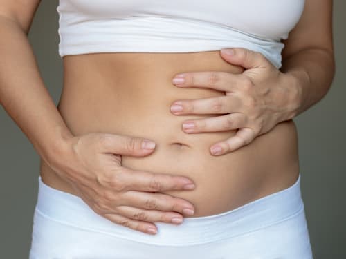A woman with gastrointestinal problems clutching her disdended abdomen.