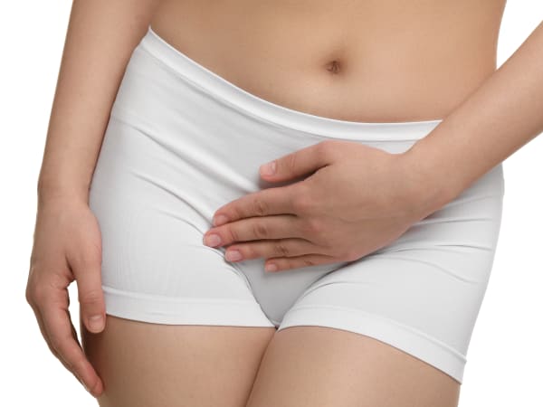 A woman in white lycra shorts holding her pelvic area in discomfort