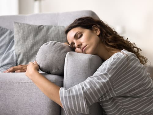 A young woman sitting on the floor, slumped against the side of a couch from tiredness.
