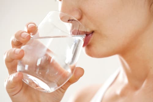 Close-up of a person's lower face as they drink from a clear glass of water