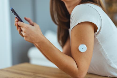 Close up of a continuous glucose monitor on a woman's arm.