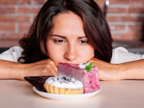 A woman struggling to resist the temptation of highly palatable sweet foods on a plate.