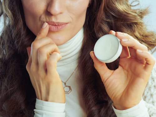 Woman applying natural lip balm for dry lips in soft natural lighting