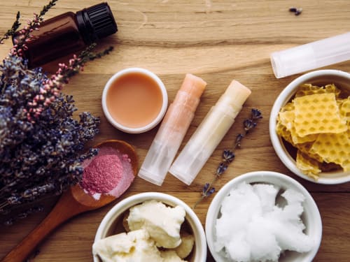 Natural lip care ingredients including shea butter, beeswax, and plant oils arranged on wooden surface