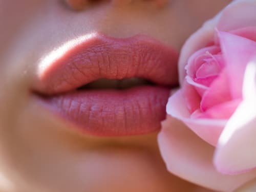 Close up of a young woman's natural, plump, hydrated lips next a light pink rose