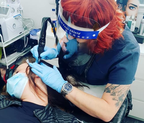Zoe carrying out hair and scalp micropigmention on a client. The client is laying on her side and the tattoo needle is applying pixels of ink to the scalp
