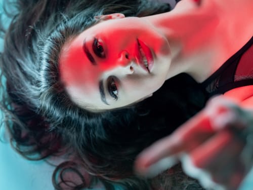 A woman laying on a blue background, her skin bathed in red light.