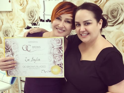 Zoe Bayliss holding her QC Brows training certificate and smiling after graduating in 2017. Standing next to Joanne Lee.