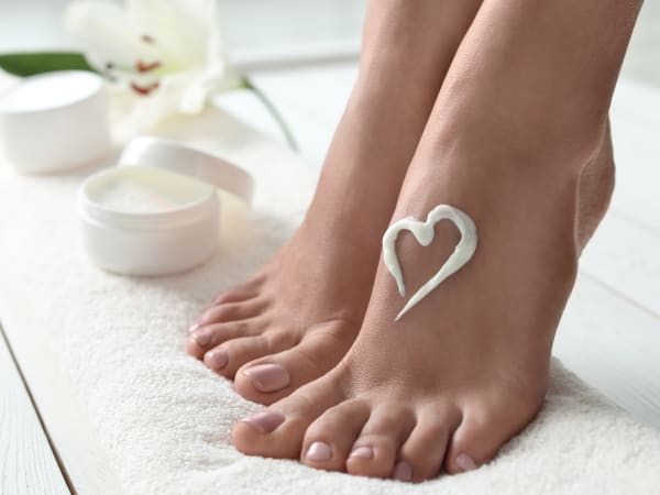 Beautiful woman's feet resting on a soft towel after a pedicure. Moisturising lotion has been placed on one foot in the shape of a heart.
