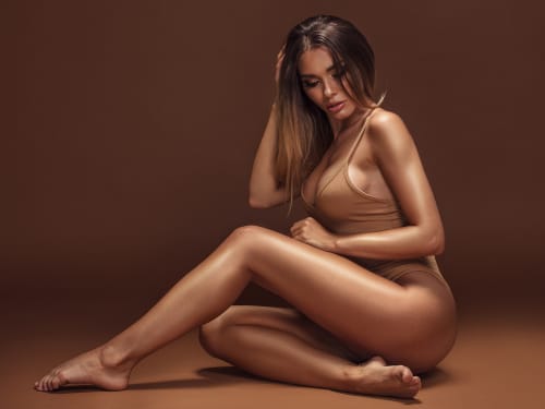 An attractive female model with a flawlessly tanned body, sitting on the floor